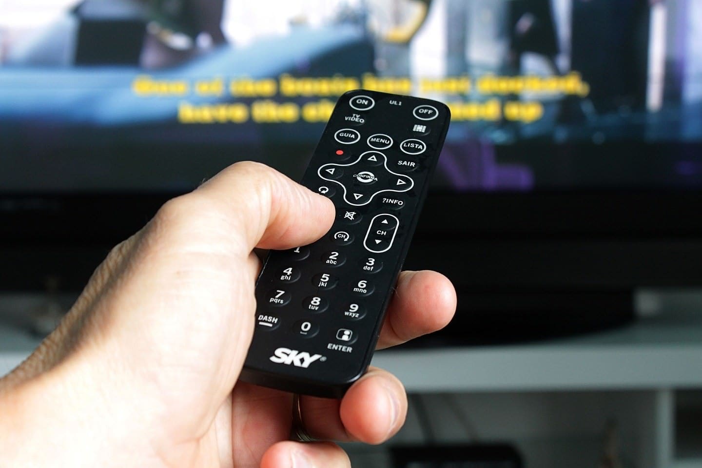 Viewer pointing remote control towards television set showing captions