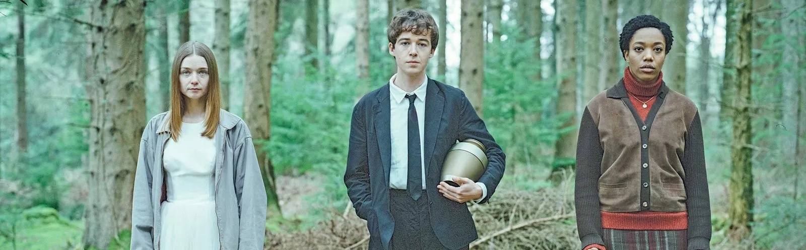 Three characters from the show The End of the F***ing World stand in a line in front of a stand of trees.