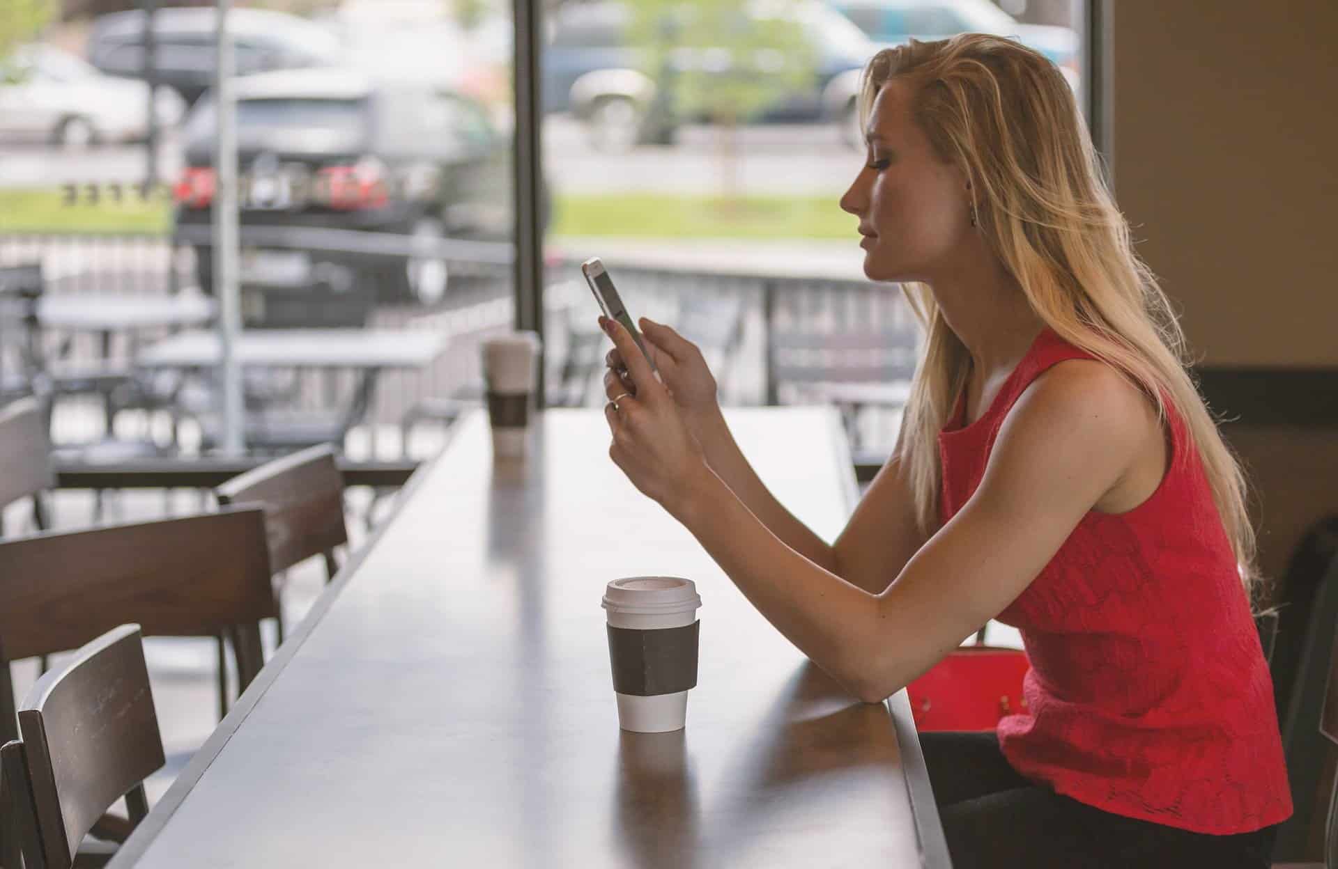Woman watching video on her mobile phone at a coffee shop counter for budgeting accessibility blog