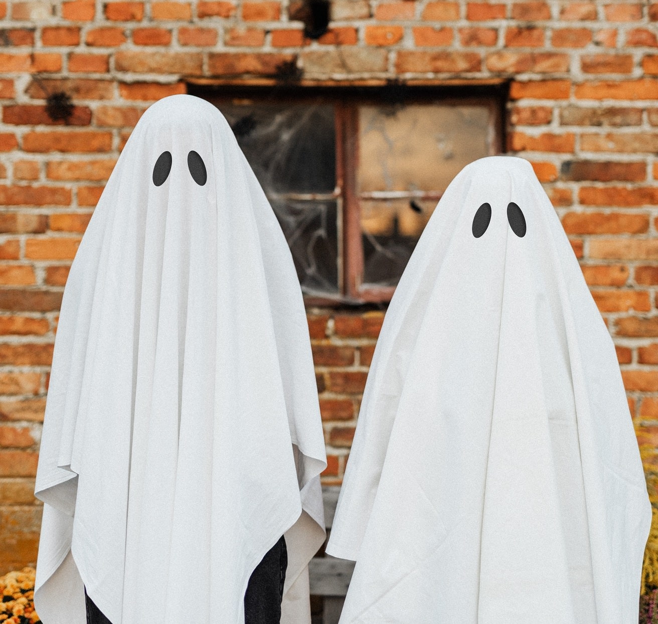Children standing in front of a brick wall wearing homemade ghost costumes
