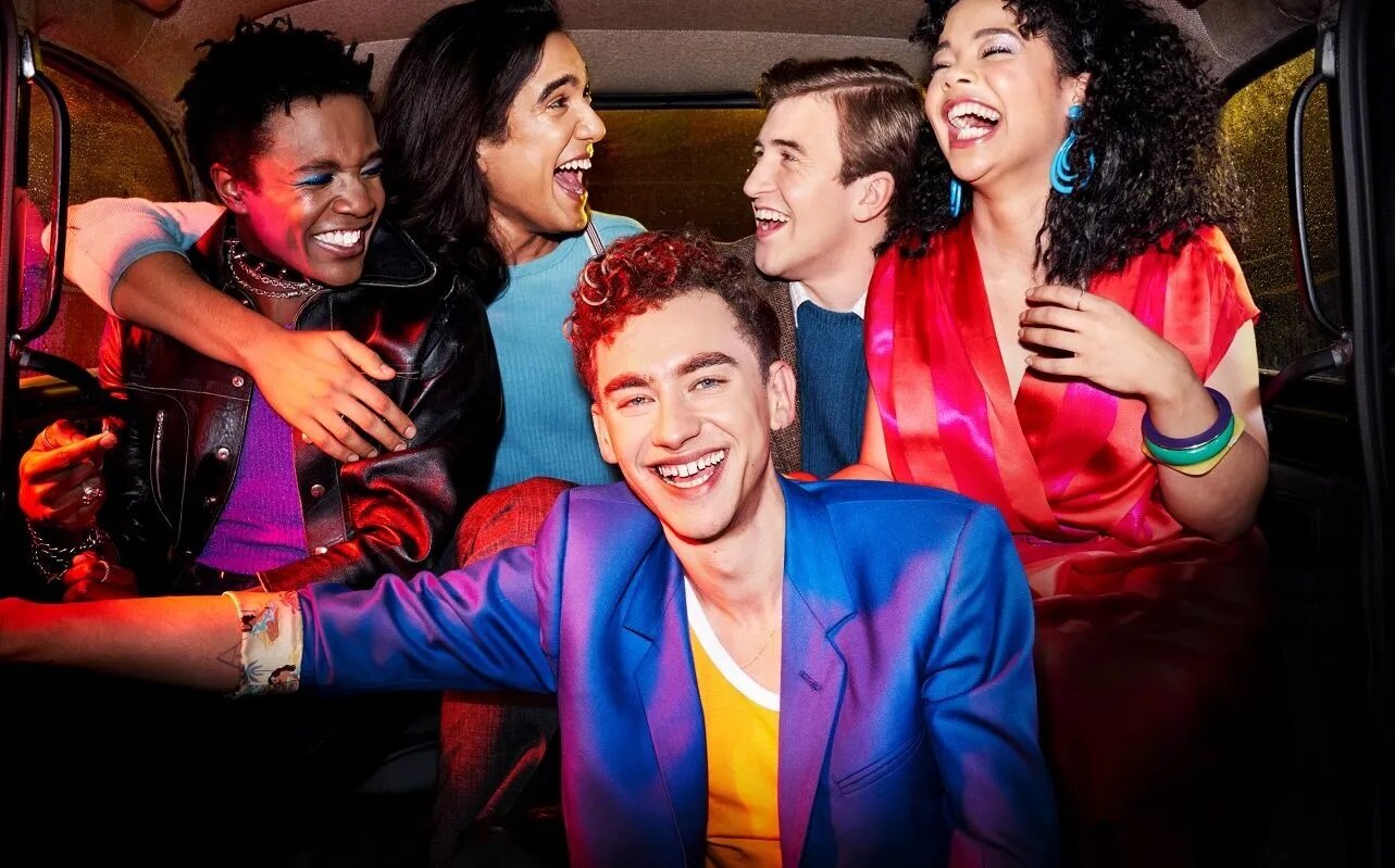 A group of young adults in brightly colored clothes seated inside a car
