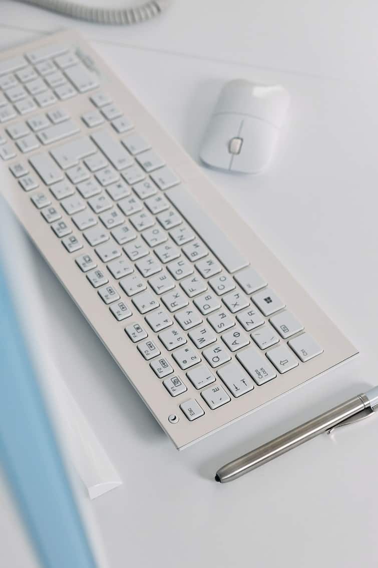 overhead view of a white computer keyboard and mouse on a desk.