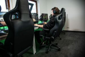 A gamer sits in a chair in front of multiple computer screens with his hands on a keyboard.