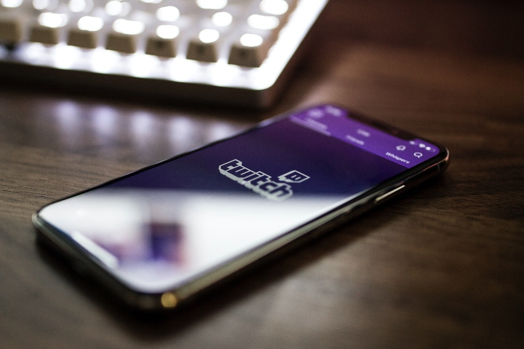 Cell phone laying on a desk near a computer keyboard with the Twitch logo displayed on the phone screen
