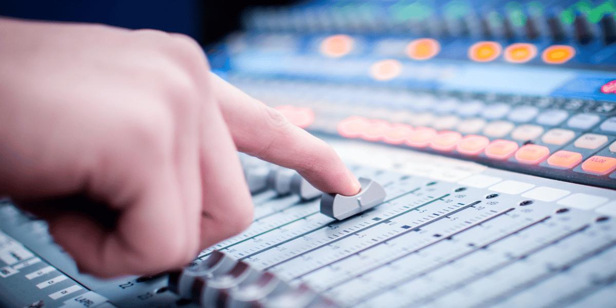 An image of a hand on a light, mixing desk fader.
