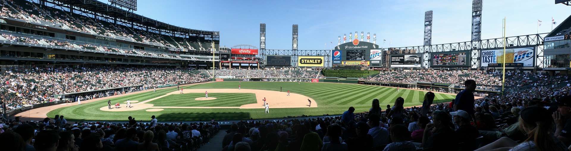 View of a packed baseball stadium from the first base line. A blue sky in the distance over the left field wall.