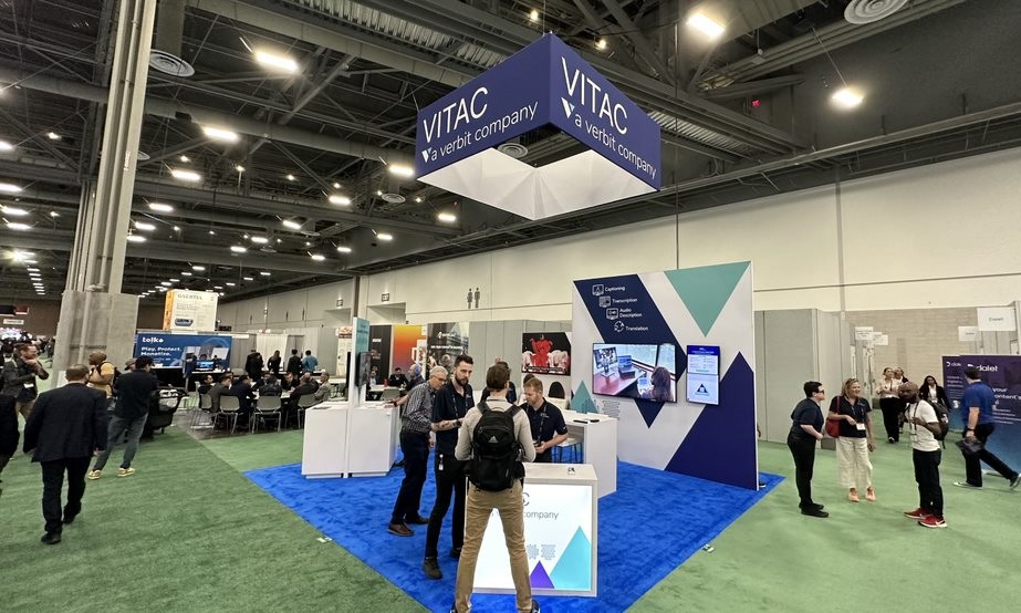 VITAC Booth on the NAB Show floor. Booth is blue and white with a large blue four sided sign hanging above reading VITAC, a Verbit Company.