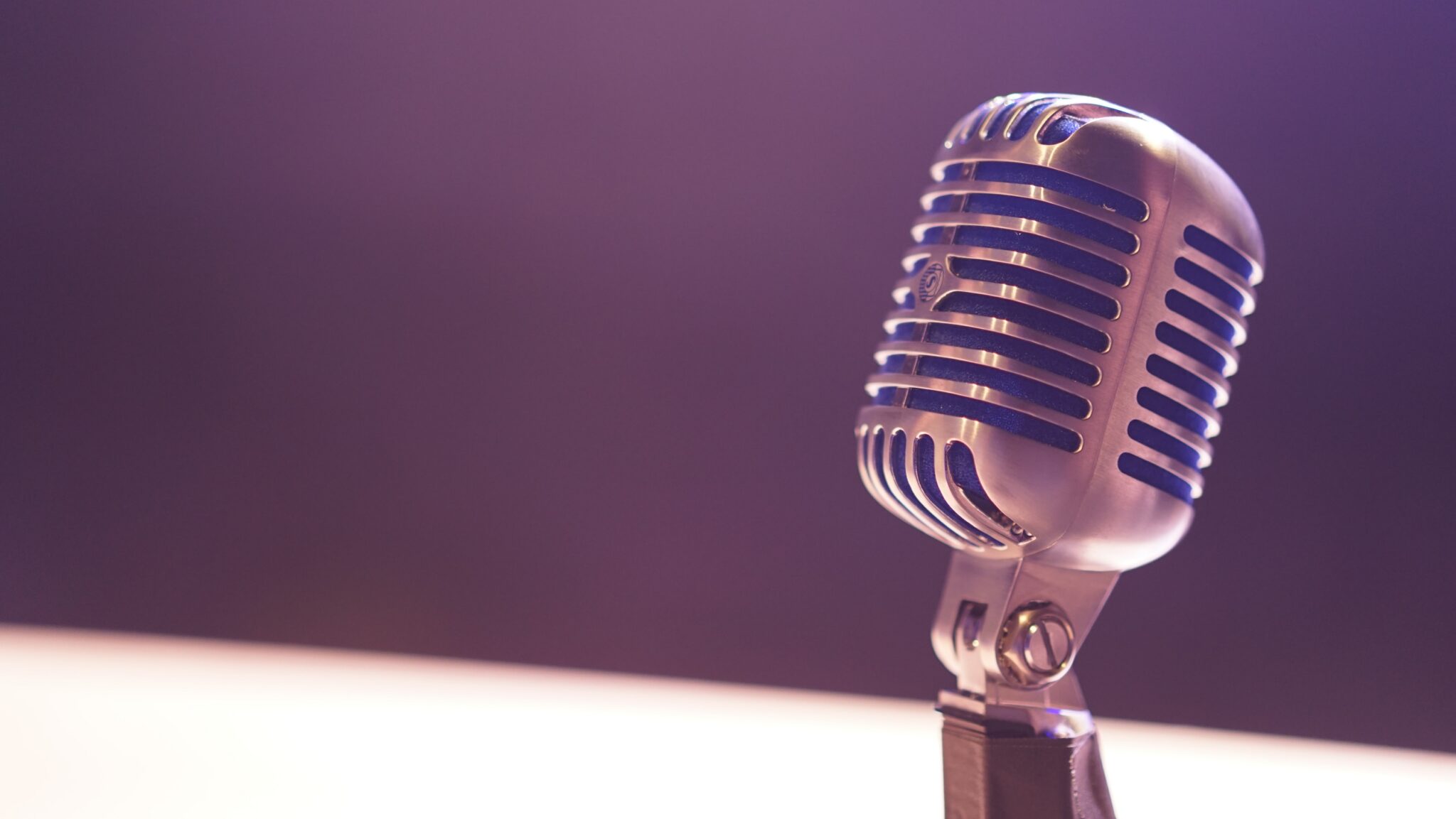 A podcast microphone stands alone in front of a purple background