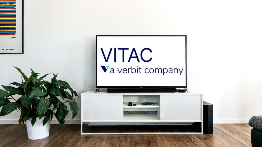 VITAC, a Verbit Company logo, on a television screen. The screen is atop a white cabinet against a white wall backdrop.