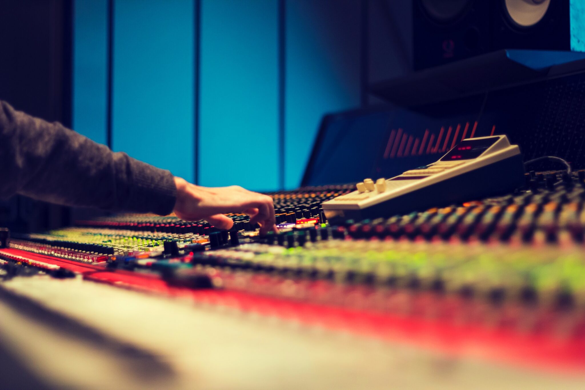 A horizontal photo of a hand operating a studio mixing board.