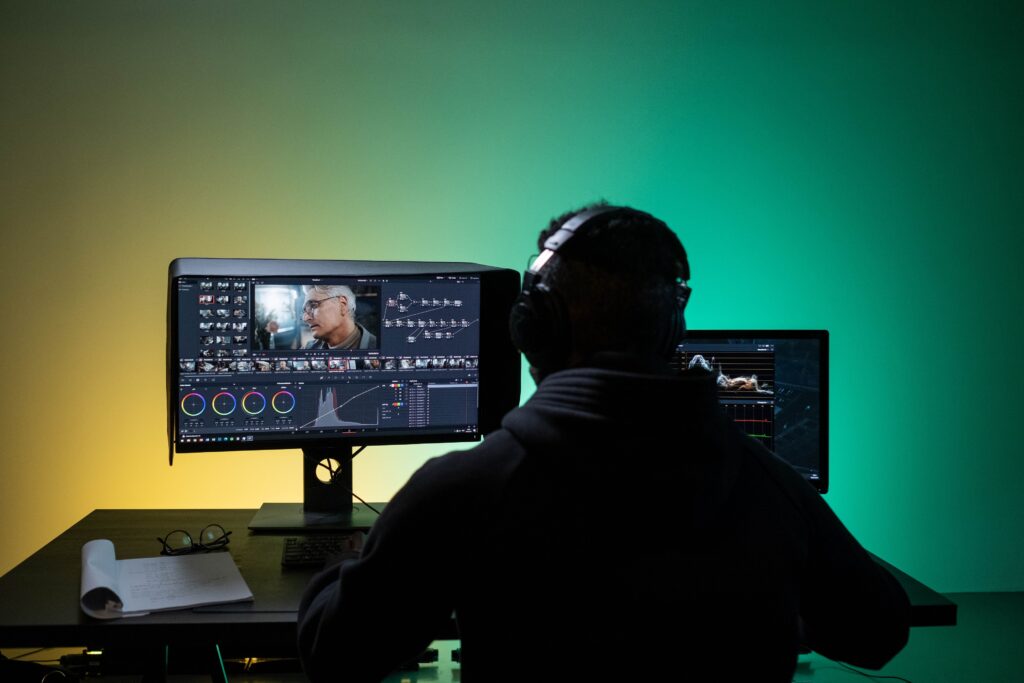 The silhouette of a man wearing headphones sitting in front of a computer screen.