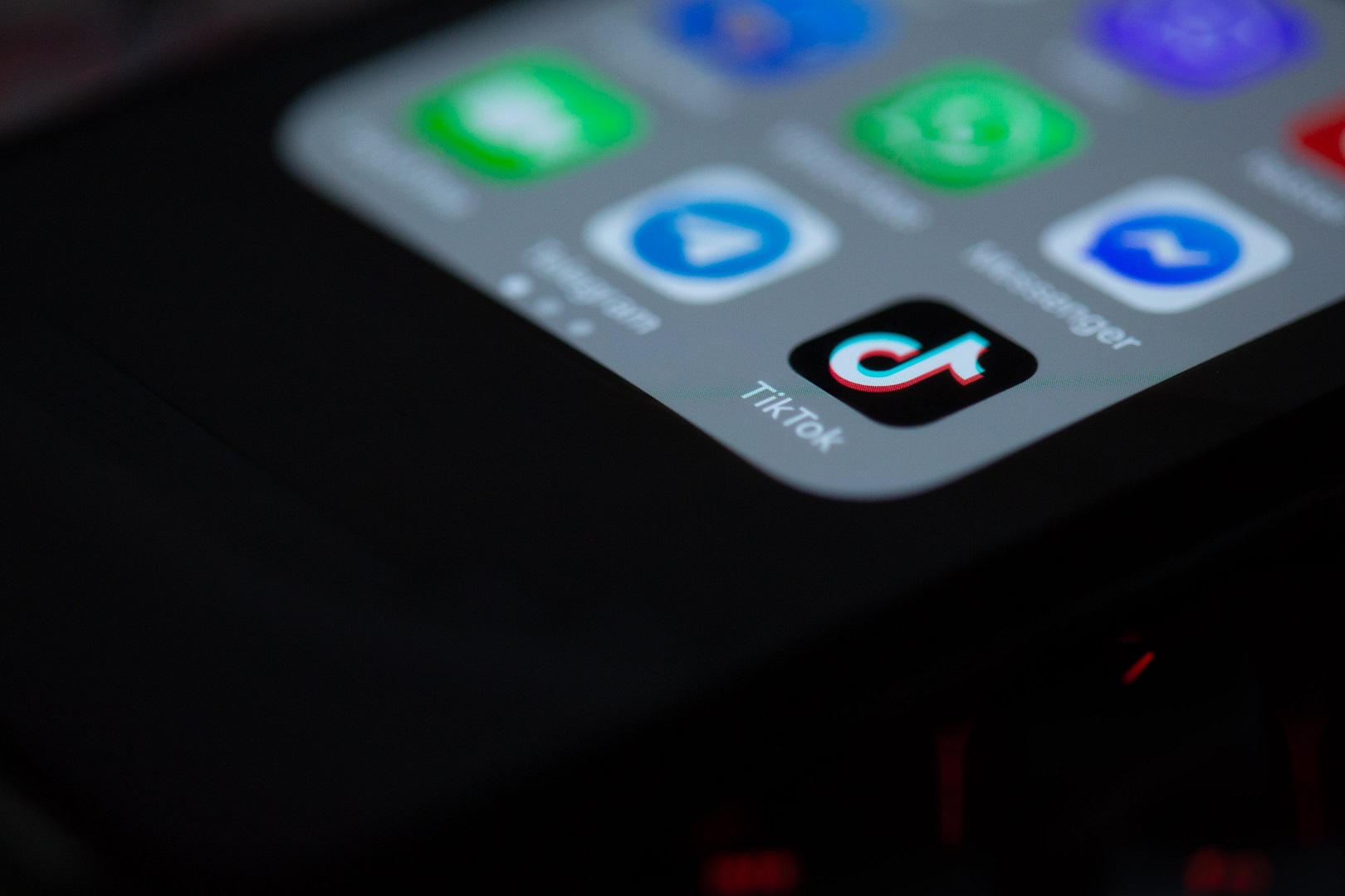 A cell phone screen against a black background. App icons appear on the screen in blur but on the bottom right of the screen, the TikTok app can visibly be seen.