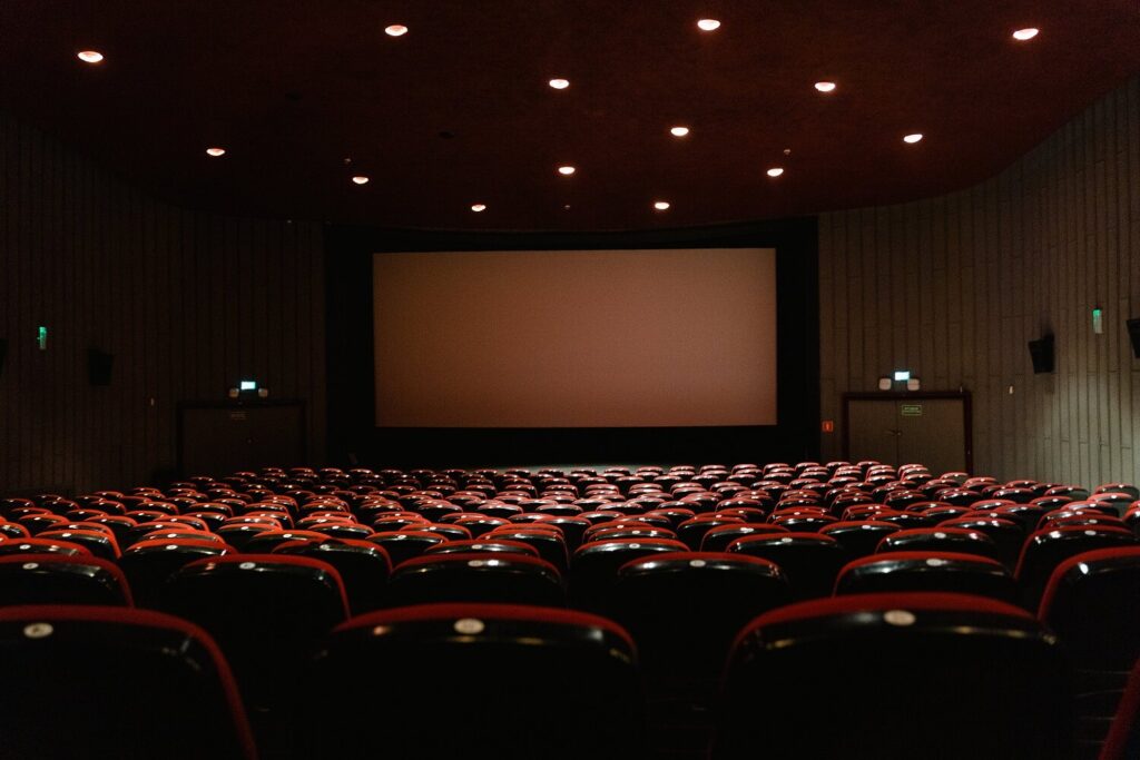 Wide view of the inside of a darkened movie theater. The silver screen in front of the audience