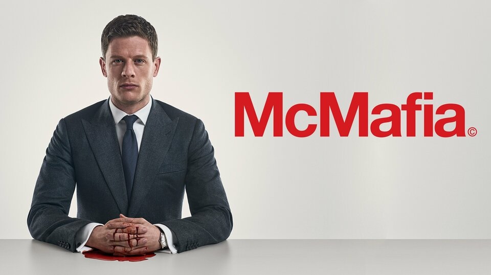 A man in a gray suit sits at white desk with his hands folded in front of him. There is bright red blood on his hands. In red letters to his left is the title 'McMafia'