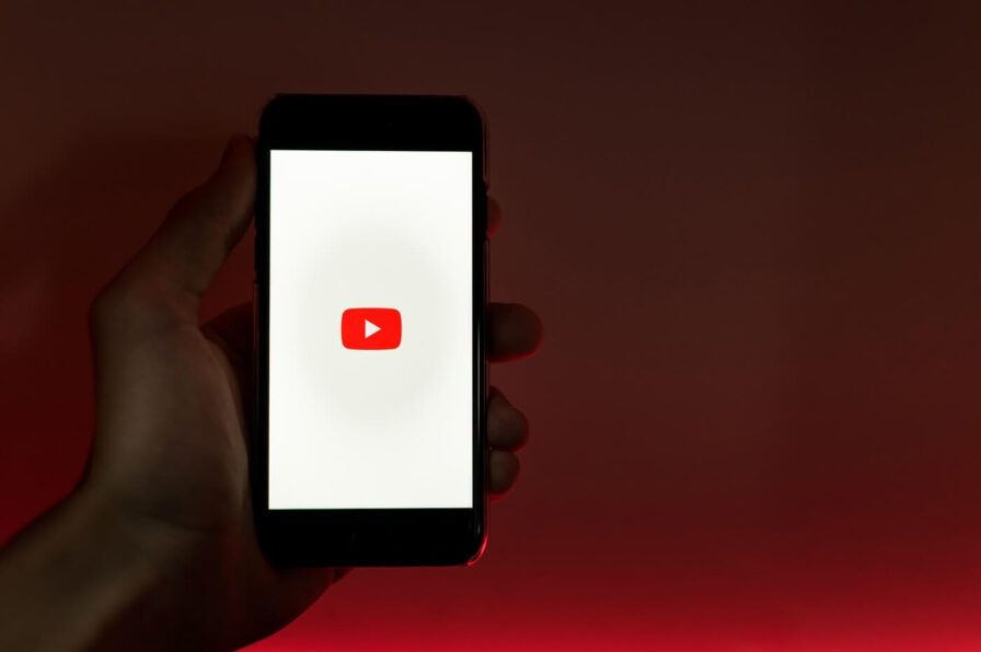 A hand hold a cell phone with the YouTube logo on the screen