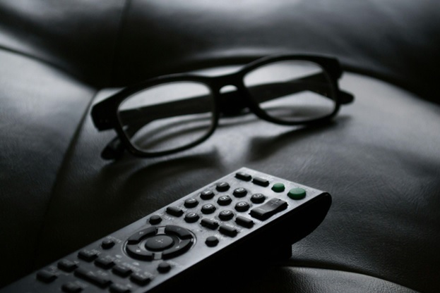 A pair of glasses rests next to a remote control on a leather couch cushion for audio description blog