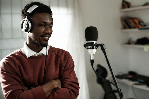 A man wears a headset and stands in front of a microphone stand.