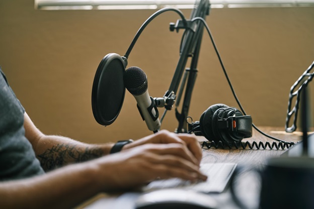 A man sits at a desk, only his hands are visible. On the desk is a microphone and headset