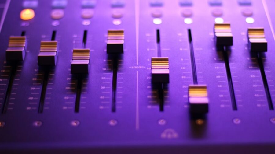 An audio mixing board is bathed in a purple light