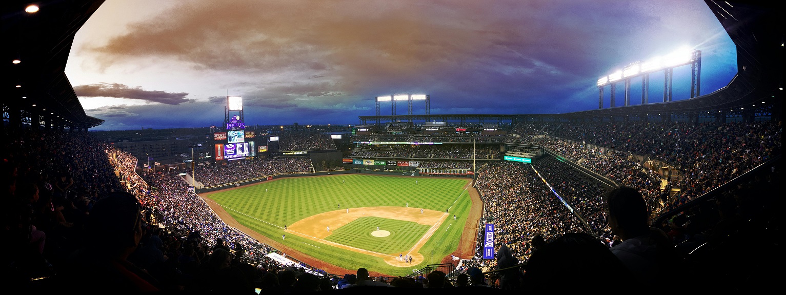Wide view of the Colorado Rockies baseball stadium, full of fans, as the sun sets in the distance.