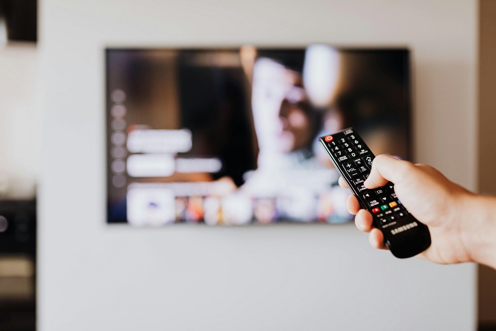 A hand points a remote control at a blurred television screen