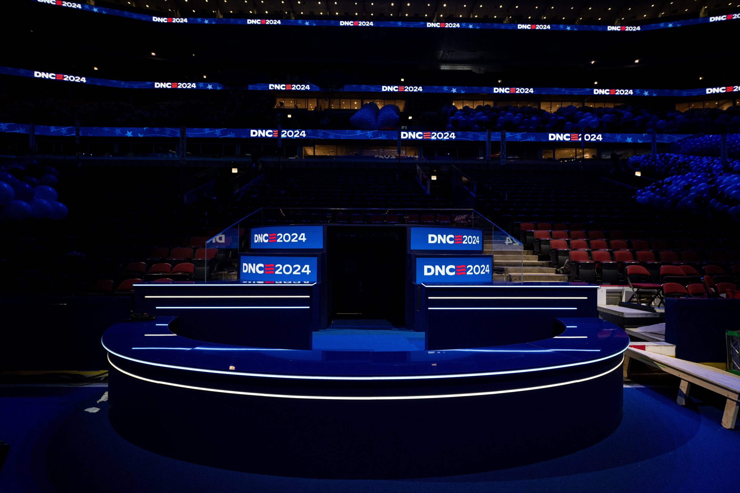 Interior of the darkened United Center with backlight signs, lit in blue, reading 'DNC 2024'