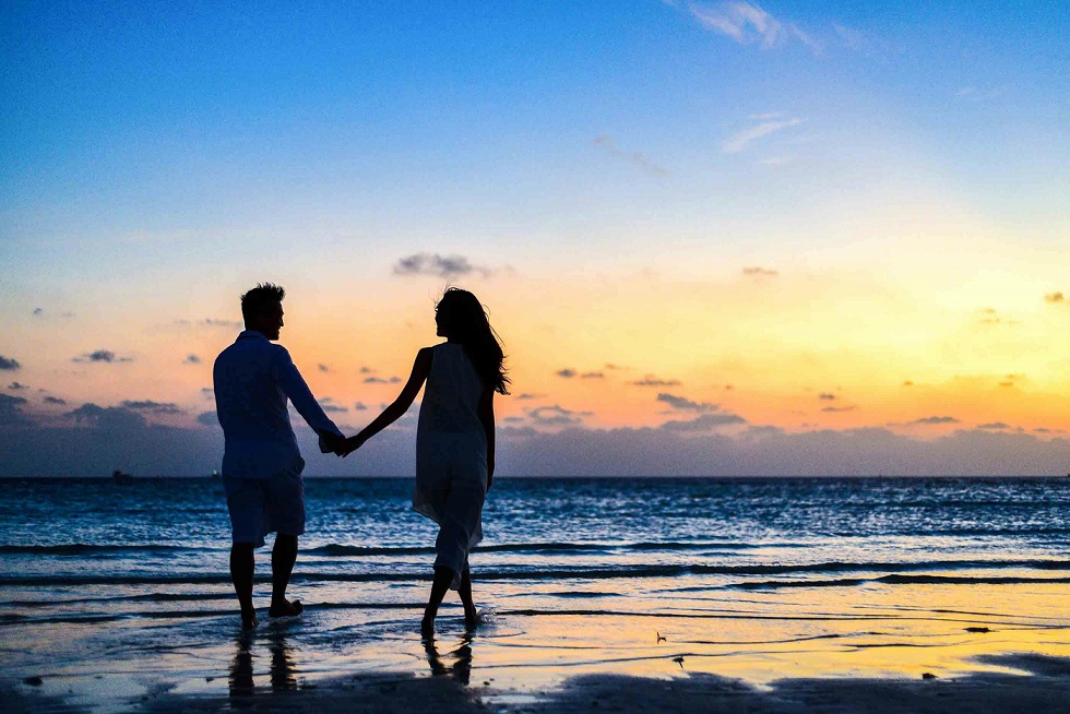 A couple in silhouette walks along a beach.