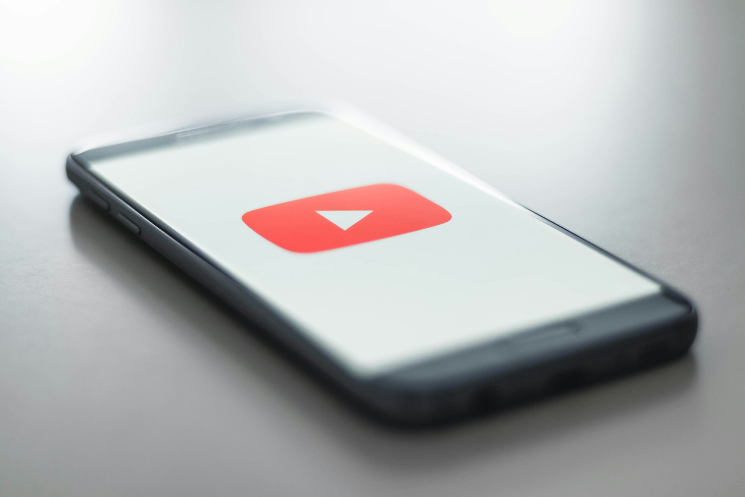 A cell phone displays YouTube's red logo with a white triangle in the center